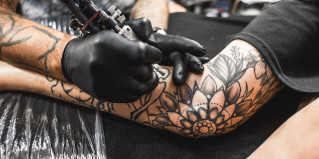 girl with dreadlocks in a tattoo parlor. The master creates a picture on the body of a young beautiful girl. Close-up of hands and tattoo machine